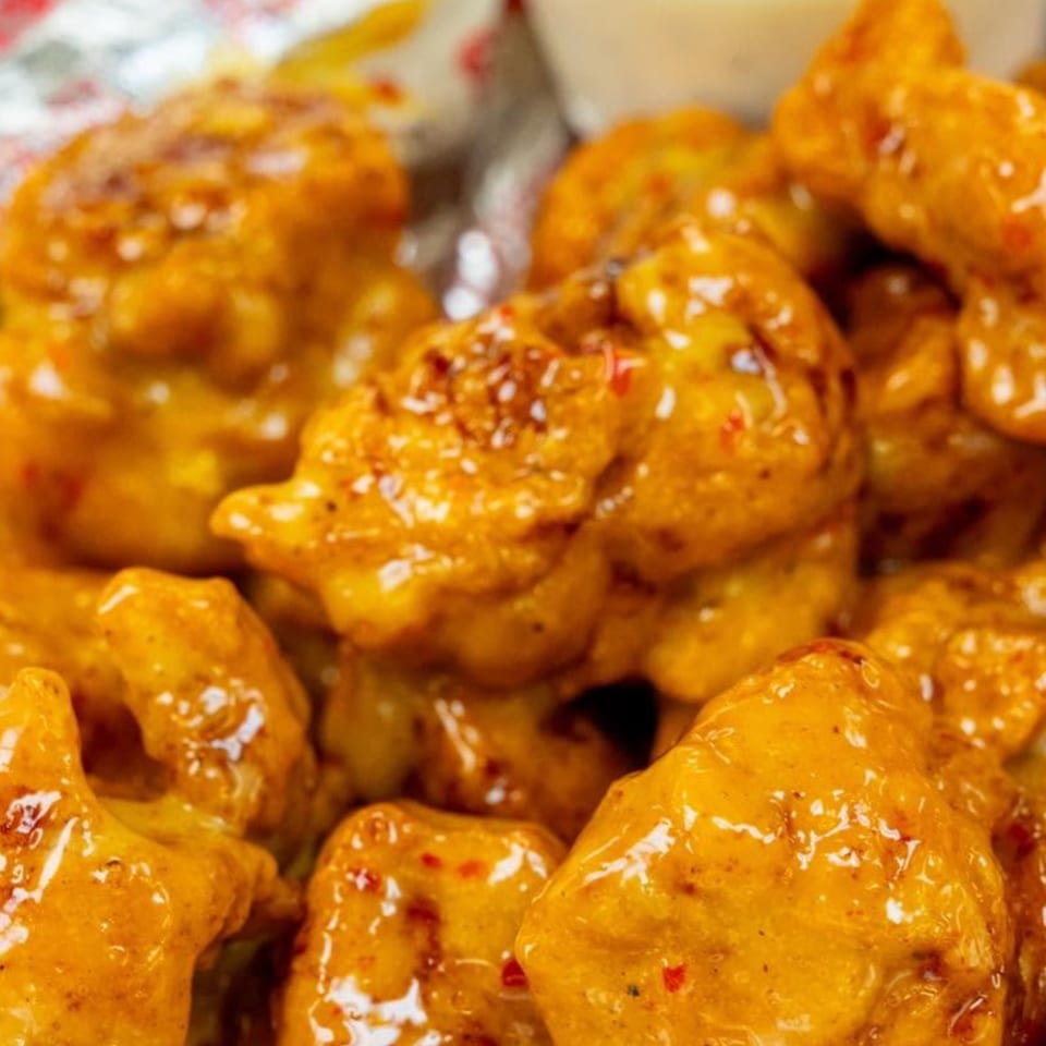 Close-up of golden-brown boneless chicken wings coated in a glossy, spicy sauce with red flakes.