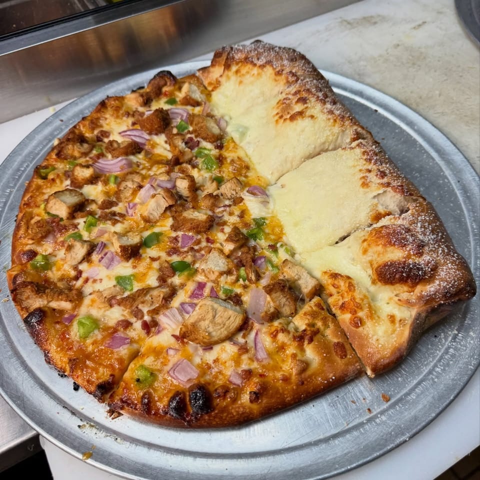 Half chicken and vegetable pizza, half cheese calzone on a metal tray.